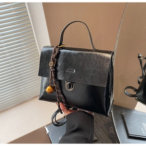Détail d'un sac à main vintage en cuir noir avec fermoir en métal et pendentif tissé