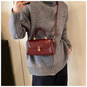 Detailed view of dark red vintage square bag with glossy finish and gold metal clasp