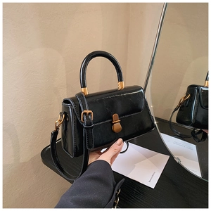 Detail of glossy black vintage handbag with golden buckle and mirror reflection finish