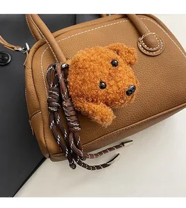 Close-up of a teddy dog plush charm hanging on a brown pebbled leather shoulder bag