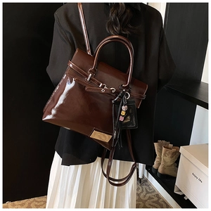 Detail of dark brown glossy patent leather handbag with leopard charm and metal clasp