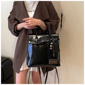 Detail of glossy black leather backpack with metallic buckle and stylish charms