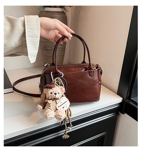 Détail d'un sac à main en cuir marron foncé avec doubles anses et charm ours peluche