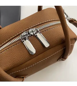 Detail view of smooth dual silver zippers on brown lychee texture leather bag top