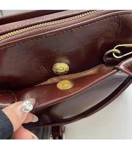 Gros plan du sac en cuir bordeaux avec fermoir magnétique doré et grainé fin