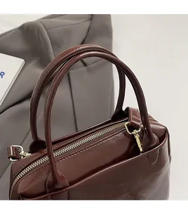 Détail d'un sac cabas en cuir marron brillant avec poignées rondes et garniture dorée
