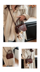 Détail d'un sac Boston en cuir marron foncé avec un pendentif ours et une bandoulière