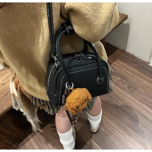 Detail of black bowling bag with white contrast stitching and a brown plush dog charm