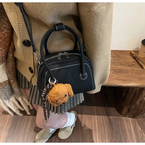 Détail du mini sac bowling noir avec coutures blanches et breloque nounours