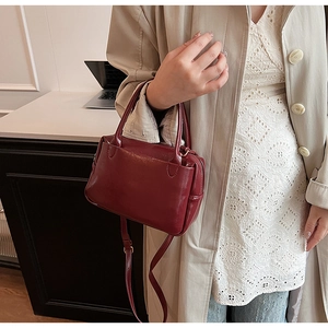 Detail einer burgunderroten Lederhandtasche mit Doppelgriffen und Schultergurt