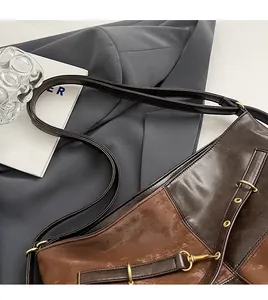 Détail d'un sac bandoulière en cuir marron brillant avec anneaux en métal et rivets