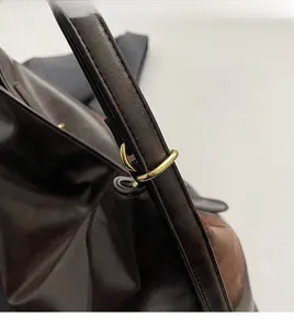 Vue détaillée des ferrures dorées et des coutures sur un sac cabas en cuir foncé