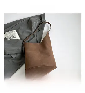 Detail view of brown suede bucket bag with vertical stitching and metal buckle