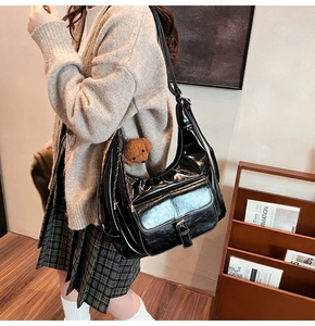 Detail of black PU leather tote bag with flap closure and brown teddy bear charm