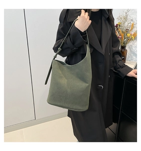 Detail of sage green suede tote bag with adjustable strap worn with a black coat