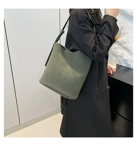 Detail of dark green suede bucket bag with vertical stitching and adjustable strap