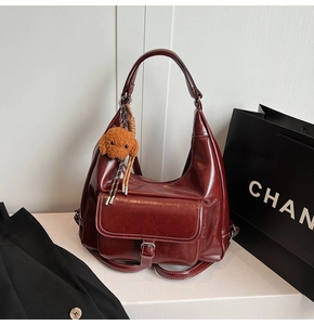 Detail of burgundy leather shoulder bag with vintage buckle and plush dog pendant charm