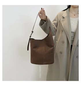 Close-up of brown suede bucket bag featuring adjustable strap and metallic buckle detail