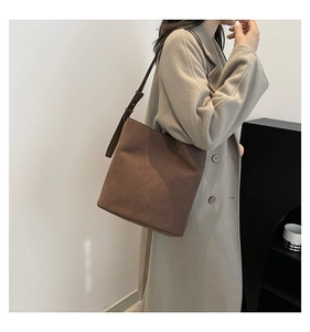 Detail of a brown suede bucket bag with adjustable leather strap and decorative stitching