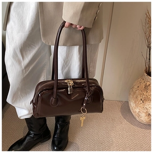 Detail of dark brown patent leather handbag with gold hardware and lock charm accessory