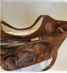 Top view of smooth gold zipper closure and interior lining on dark brown glossy tote bag
