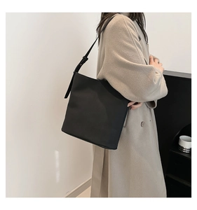 Minimalist black tote bag with adjustable strap shown on a model in a stylish wool coat