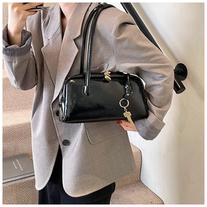 Detail of a black glossy leather handbag with thin straps and a gold key charm