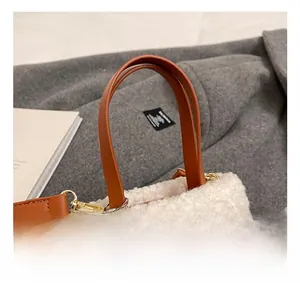 Detail of brown suede handbag with white faux fur trim and silver keychain accent