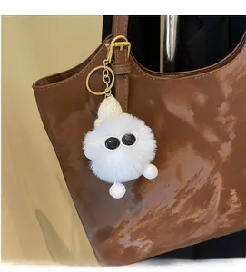 Detail of cute white plush ball keychain with mini knit hat and glasses on brown tote bag