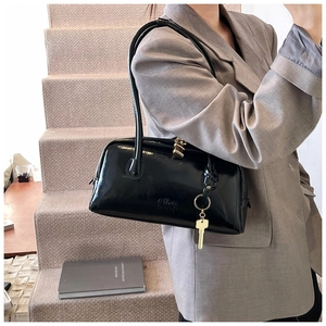 Detail view of glossy black commute bag with gold lock buckle and long shoulder strap