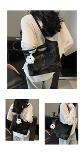 Detail of black large tote bag with oil wax texture and cute white plush monster charm