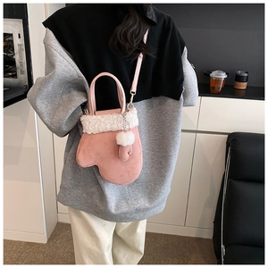 Detail of pink glove-shaped crossbody bag with white fleece trim and pompom charm