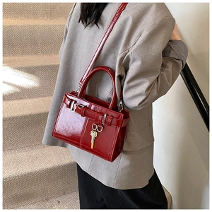 Detail of burgundy patent leather satchel featuring gold key charm and thin shoulder strap