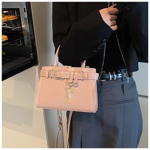 Detail view of light pink glossy handbag with metal key charm and leather strap buckle