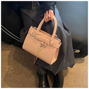 Close-up of beige-pink leather handbag featuring a golden key charm and buckle detail