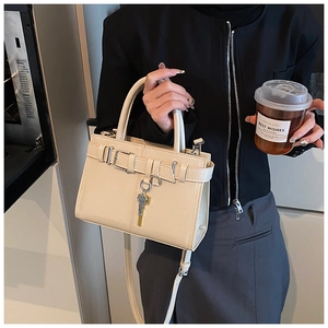 Detail of off-white structured handbag with leather belt strap and metal key pendant