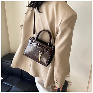 Detail of dark brown glossy leather crossbody bag with gold key pendant and shoulder strap