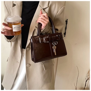 Detail of deep brown patent leather handbag with gold key charm and strap buckle