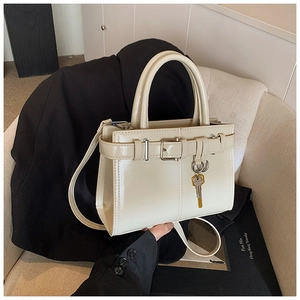 Detail of creamy white crossbody bag with glossy leather, metal buckle, and key pendant