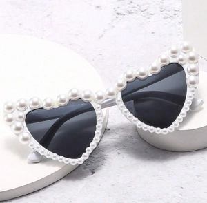 Close-up of heart-shaped sunglasses with white faux pearl embellishments and dark lenses