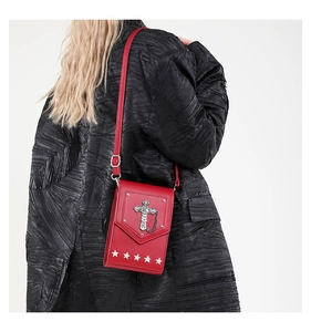 Detail of red punk crossbody bag featuring silver cross, chain, and star rivets