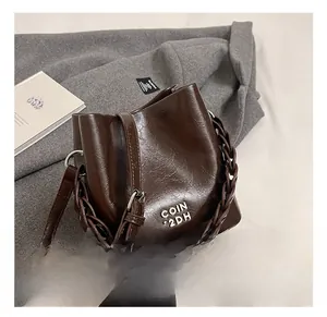 Détail du logo en métal argenté et poignée tressée sur le sac seau en cuir ciré marron