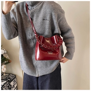 Détail d'un sac seau rouge foncé brillant avec poignée en chaîne tressée et logo métallique