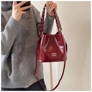 Détail du sac seau bordeaux en cuir ciré avec logo métallique et poignée tressée