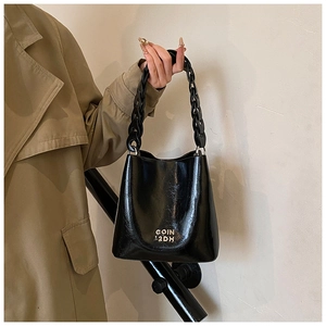 Détail du sac seau noir brillant en cuir ciré avec logo doré et bandoulière chaîne épaisse