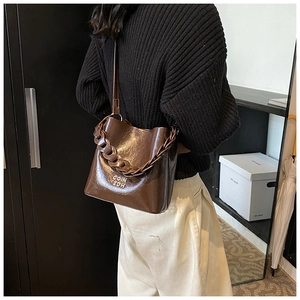 Détail du sac seau en cuir ciré marron foncé avec chaîne épaisse en résine et logo gravé