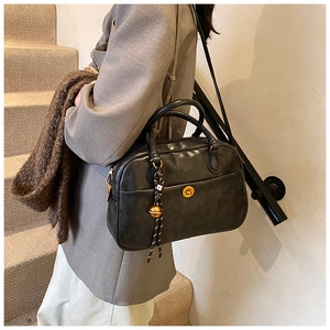 Detail of black Boston bag with golden circular twist lock and decorative bell pendant