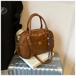 Detail of a brown leather Boston bag with a vintage gold metal twist lock and decorative cord