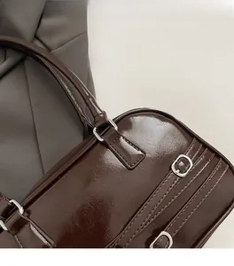 Gros plan d'un sac à main en cuir verni marron foncé avec boucles argentées