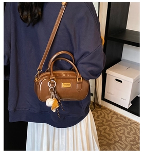 Close-up detail of brown leather Boston handbag with metal plaque and cute charms worn casually.
